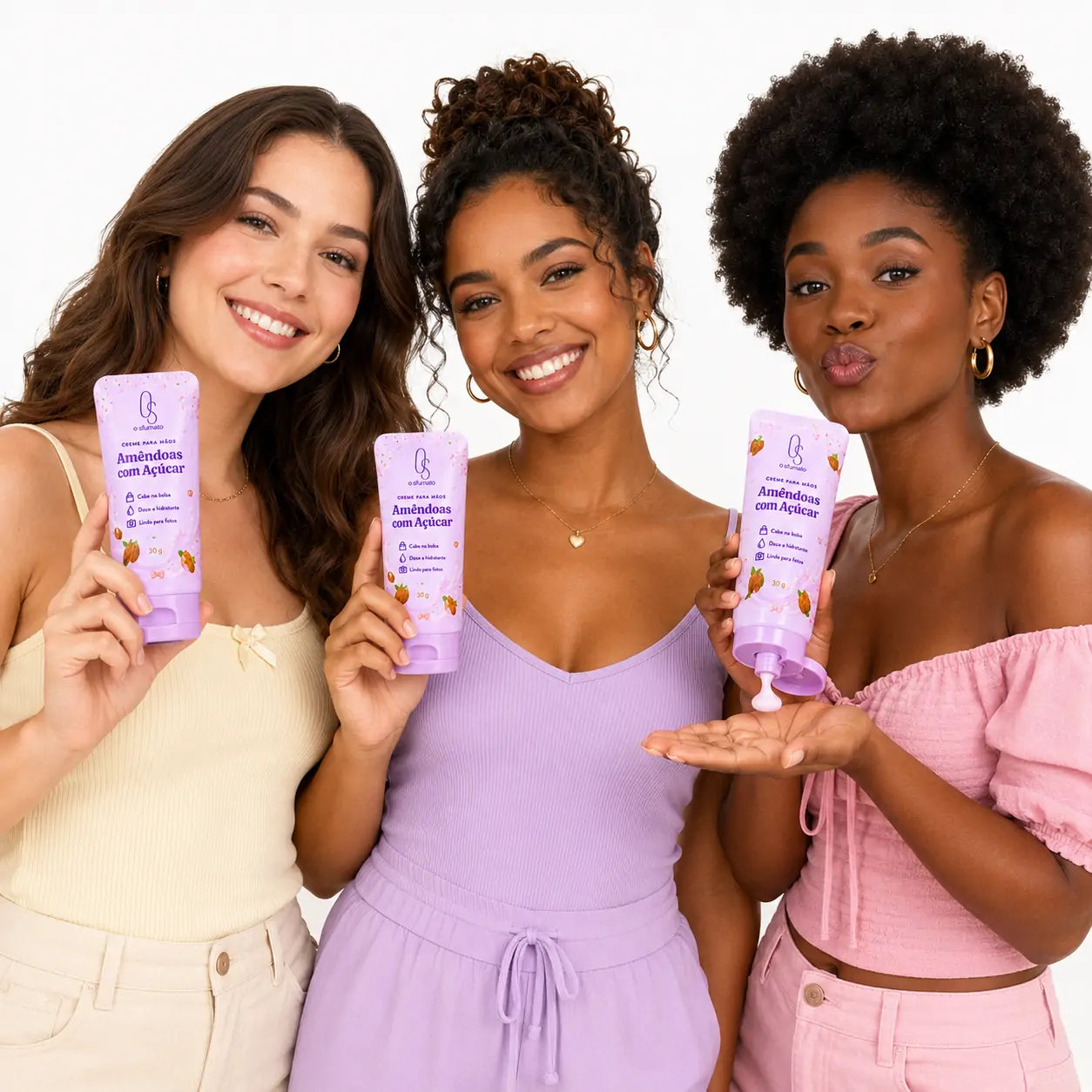 Três mulheres brasileiras de diferentes tons de pele segurando o creme para mãos O Sfumato Amêndoas com Açúcar em fundo branco.