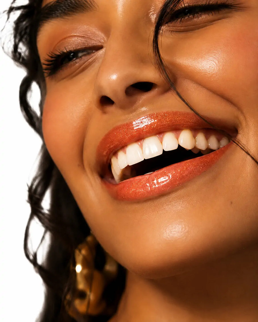 O Sfumato™ Lip Oil Coral Sunset em embalagem verde com aplicador e brilho coral alaranjado