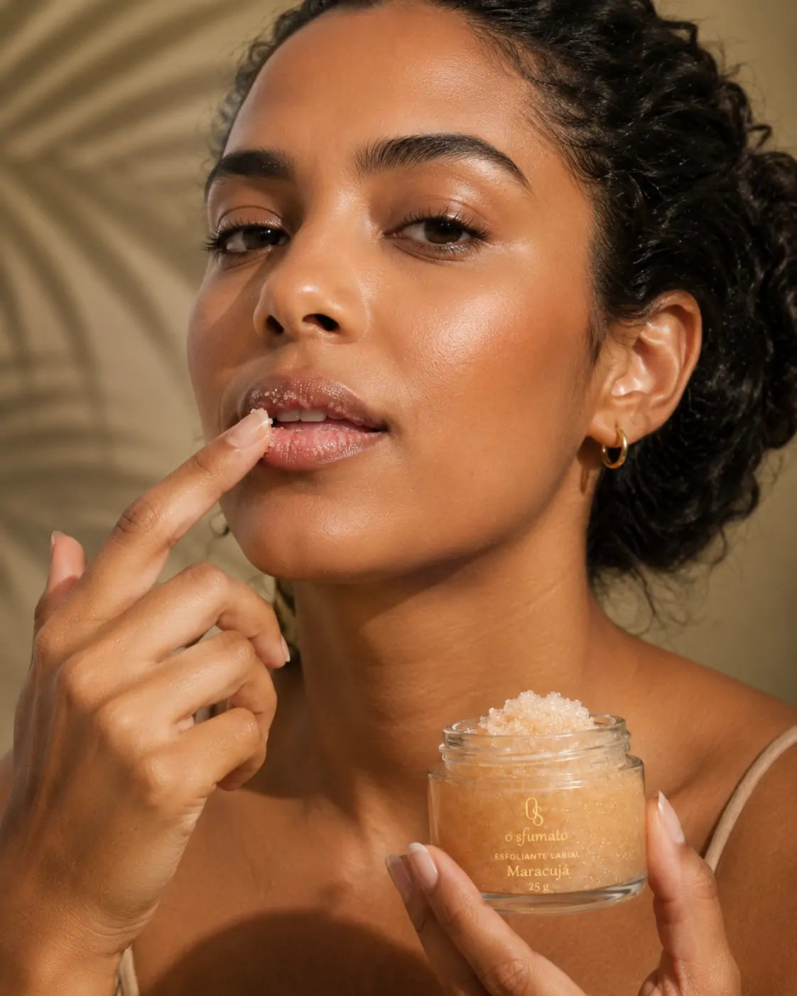 Modelo aplicando esfoliante labial O Sfumato Maracujá nos lábios com textura granulada e acabamento hidratado